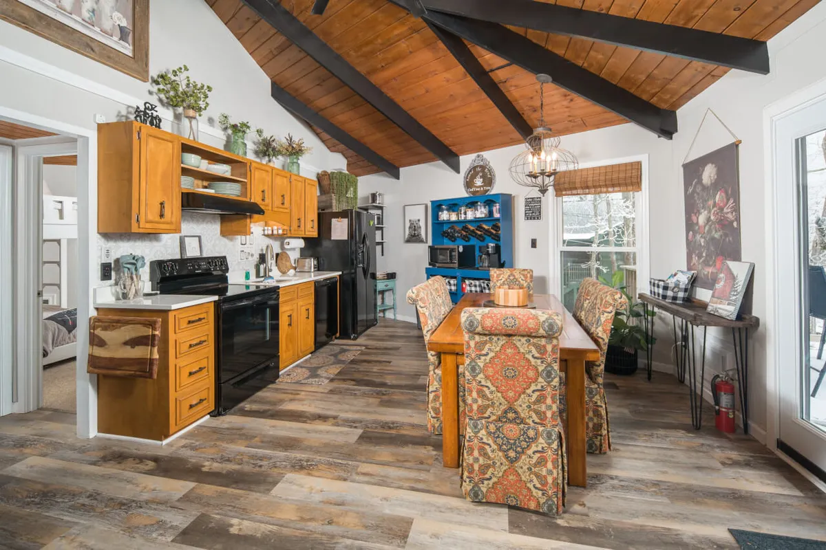 A bright, open kitchen and dining area with a kitchen island, wooden beams, colorful cabinetry, and a large dining table—suggesting a space for family meals and celebrations after a day outside. The area is well-lit and feels welcoming for groups.