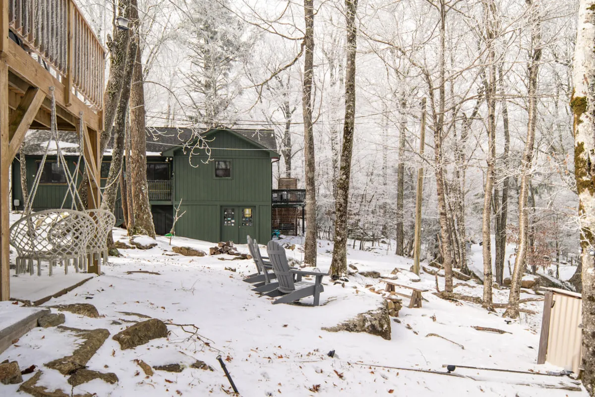 This image showcases a wooden deck surrounded by snow-covered ground and tall trees. Adirondack chairs are set up on the deck, inviting guests to relax and enjoy the peaceful mountain atmosphere. The surrounding natural landscape is visible, reinforcing a connection between indoor comfort and the outdoors.
