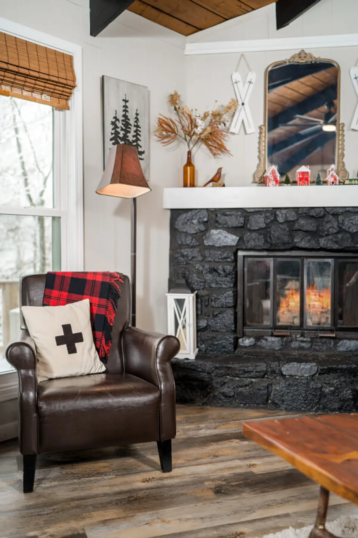 A cozy living area featuring a leather armchair placed near a stone fireplace. The mantel is decorated with charming accents, and a plaid blanket adds a touch of warmth. The space exudes a welcoming atmosphere, ideal for relaxing after exploring the nearby village.