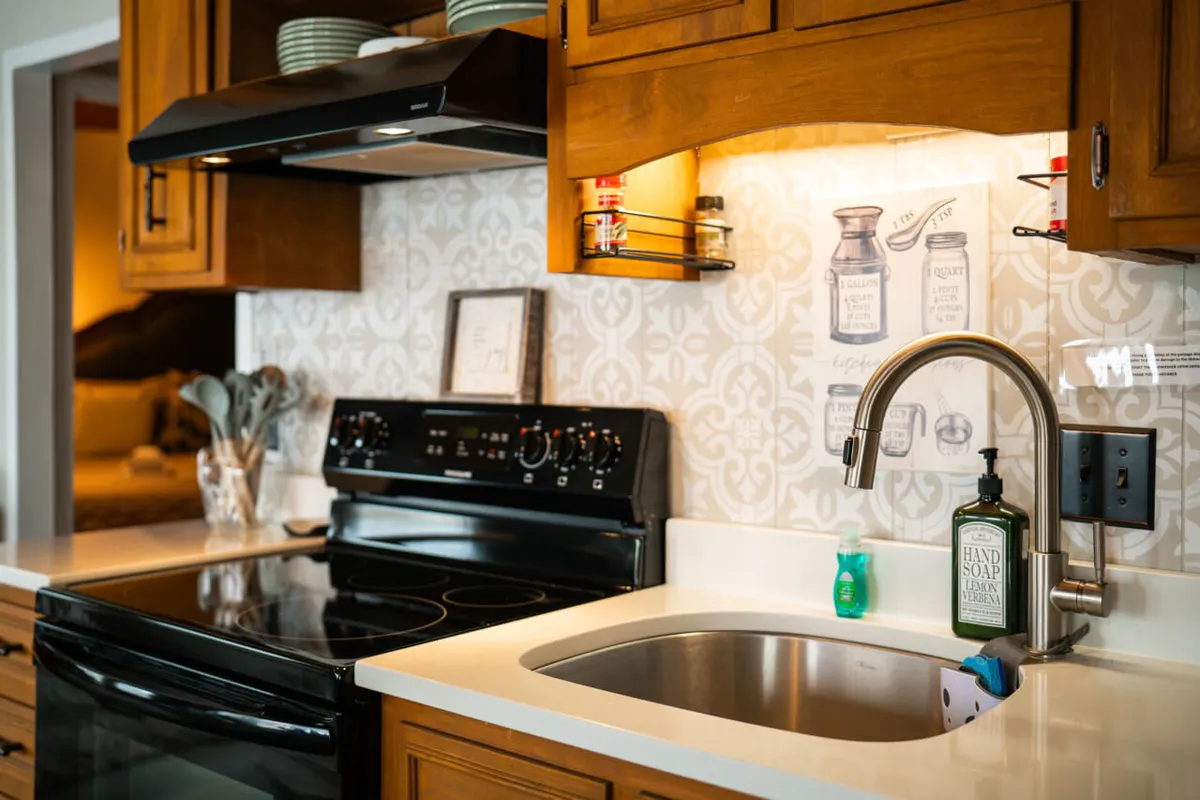 A functional yet inviting kitchen with stainless steel sink, black stove, decorative backsplash, and wooden cabinets. The space is clearly designed for both cooking and socializing, with thoughtful details that hint at family gatherings and lively meal prep.