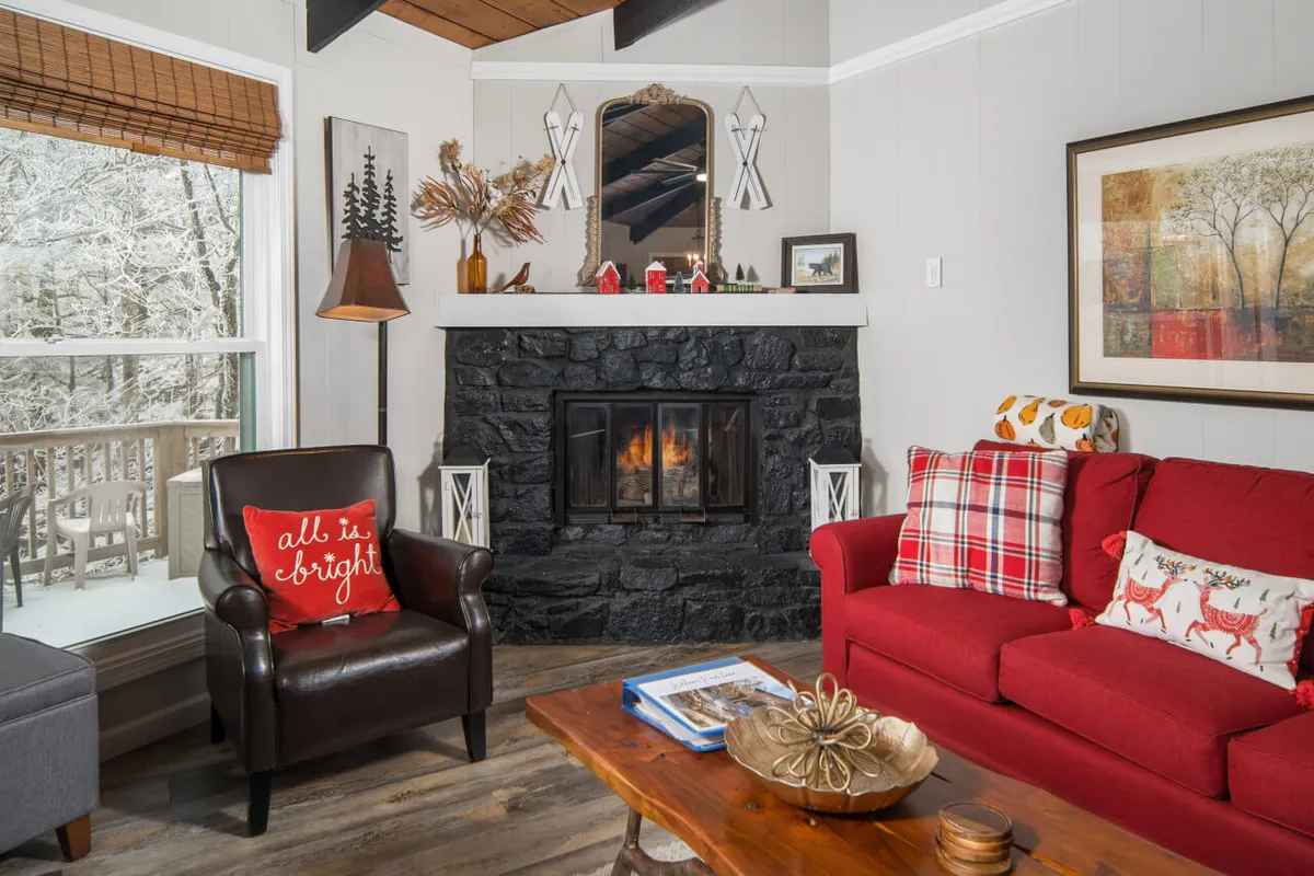 A warmly lit living space with a red sofa facing a stone fireplace, decorative mantel items, and snow-themed decor. The room radiates a welcoming, après-ski vibe, perfect for gathering after a day on the slopes or trail.