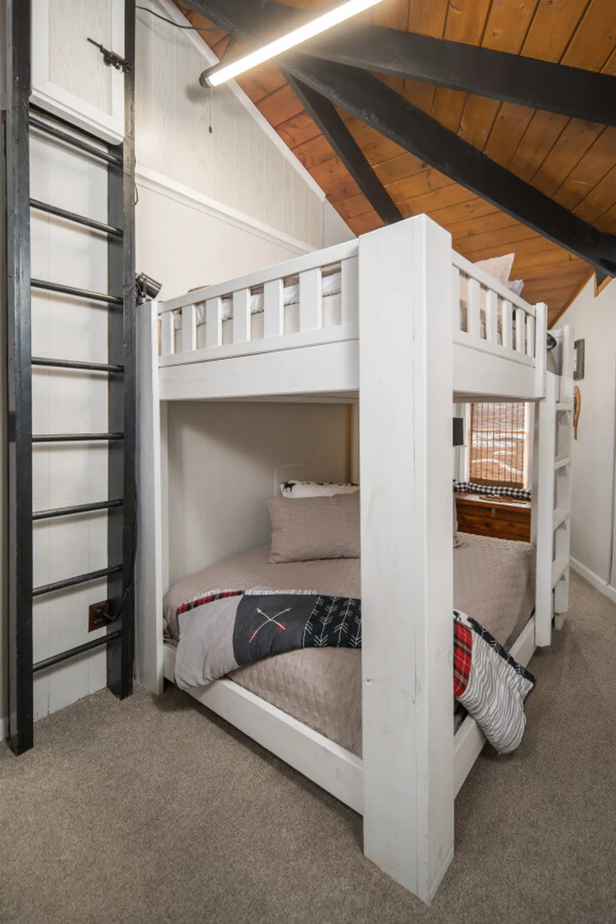 The image features a guest room with queen-over-queen bunk beds, a sturdy ladder, and cozy, textured bedding. The playful arrangement hints at a space designed for families or groups, with an inviting atmosphere for both sleep and fun.