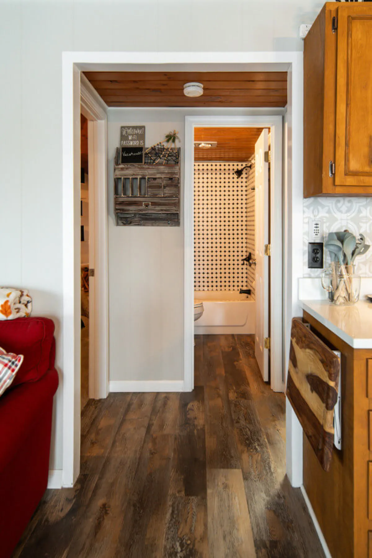 An inviting interior view featuring a rustic wooden welcome sign and glimpses of both kitchen cabinetry and a bright, patterned shower curtain, hinting at the home’s blend of comfort and convenience.