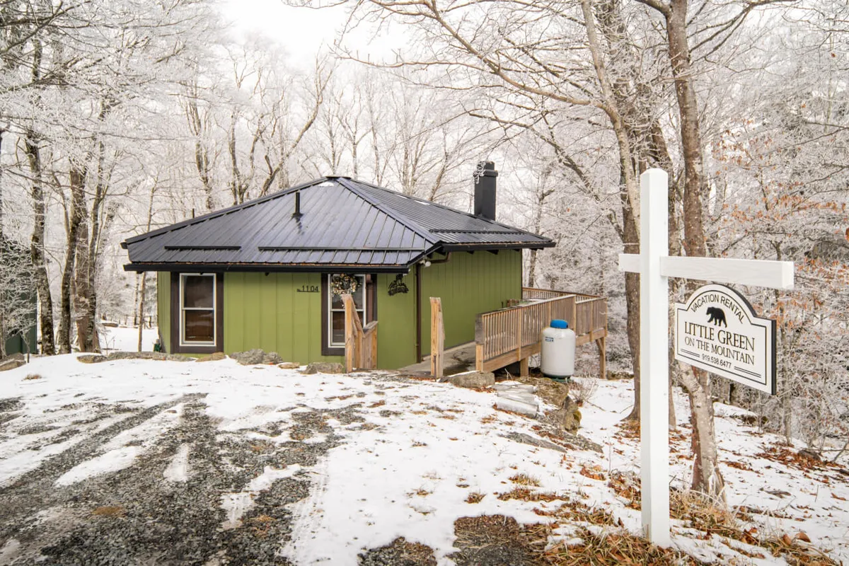 An inviting exterior shot of LittleGreen’s green cabin with a black roof and wooden deck, surrounded by snow and a wooden signpost. The scene conveys warmth and provides a glimpse of the cozy retreat waiting for families after a day on the slopes.