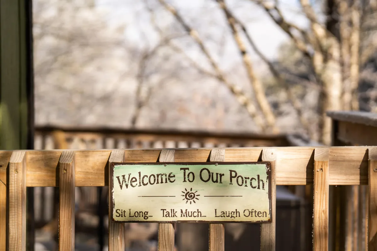 A warmly lit interior scene featuring a welcome sign mounted on a rustic wooden railing, with natural surroundings visible through the windows. The atmosphere is relaxed, with people sitting and conversing, suggesting a welcoming space for both guests and their pets.