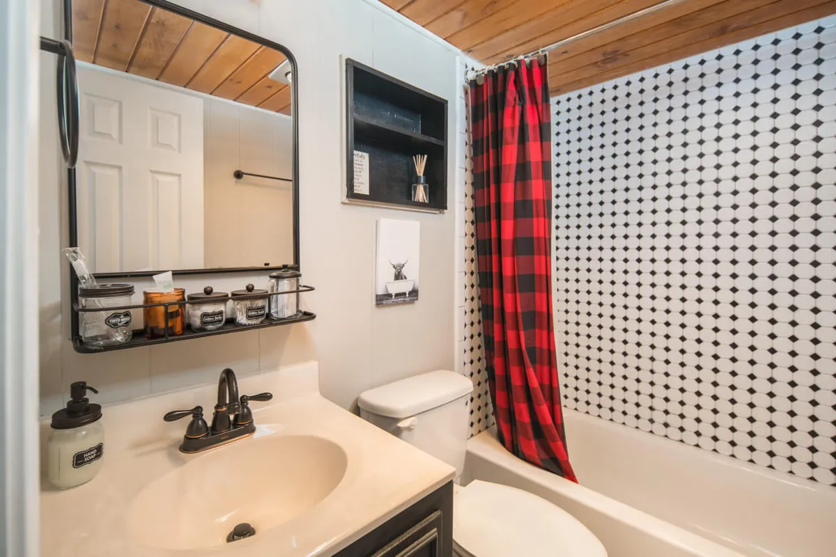 A stylish bathroom with a vanity sink, mirror, shower curtain, and black and white tiled wall. The space feels clean and inviting, perfect for relaxation and self-care routines after a day outdoors.